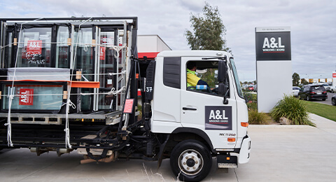 A lorry loaded with glass windows, purpose-built, is parked in front of A&L Windows signage at a commercial building under cloudy skies.