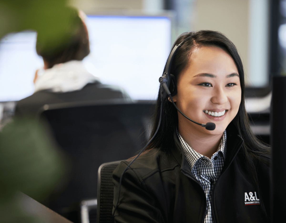 A woman wearing a headset sits at a desk and smiles at a computer screen in an office setting.