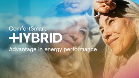 Older woman with long grey hair looks out an A&L window, her reflection visible. Overlaid text reads, ComfortSmart Hybrid—your project upgrade for superior energy performance.